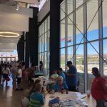 A group of people are sitting at tables in a room with a lot of windows.
