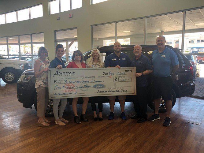 A group of people are holding a large check in front of a car.