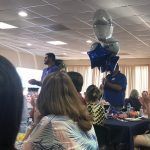 A group of people are sitting at tables in a room with balloons hanging from the ceiling.