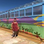 A woman in a red dress is standing next to a train on the tracks.