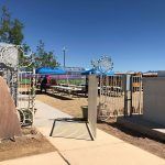 A walkway leading to a fenced in area with tables and chairs.