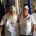 A man and a woman are posing for a picture in front of an american flag.