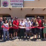 A group of people are standing in front of a building holding a red ribbon.