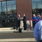 A group of people are standing outside of a building cutting a red ribbon.