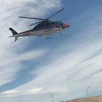 A helicopter is flying in the sky over a hill.