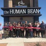 A group of people are standing in front of a building holding a red ribbon.