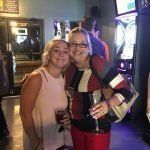 Two women are standing next to each other in a bar holding wine glasses.