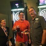 A group of people are standing next to each other in front of a dart board.