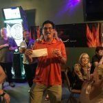 A man is standing in front of a group of people in a bar holding a check.