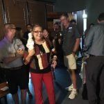 A group of people are standing around a woman holding a remote control in a room.