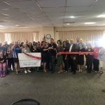 A group of people are standing in a room holding a red ribbon.