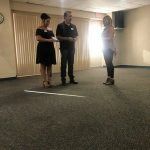 A man and two women are standing in a room talking to each other.