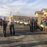 A group of people are standing in front of a row of golf carts.