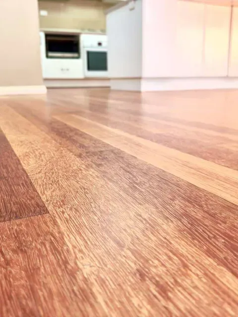 Close-up of a polished wooden floor in a kitchen, with a glimpse of an oven and cabinets in the background.
