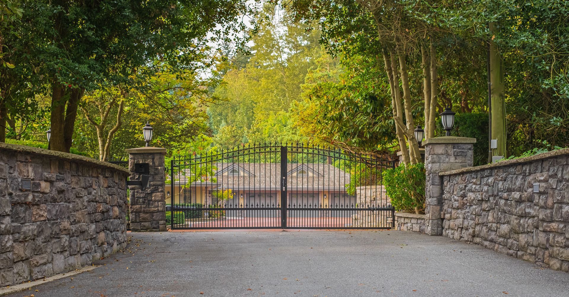 Wrought iron gate between stone walls leading to a private residence.