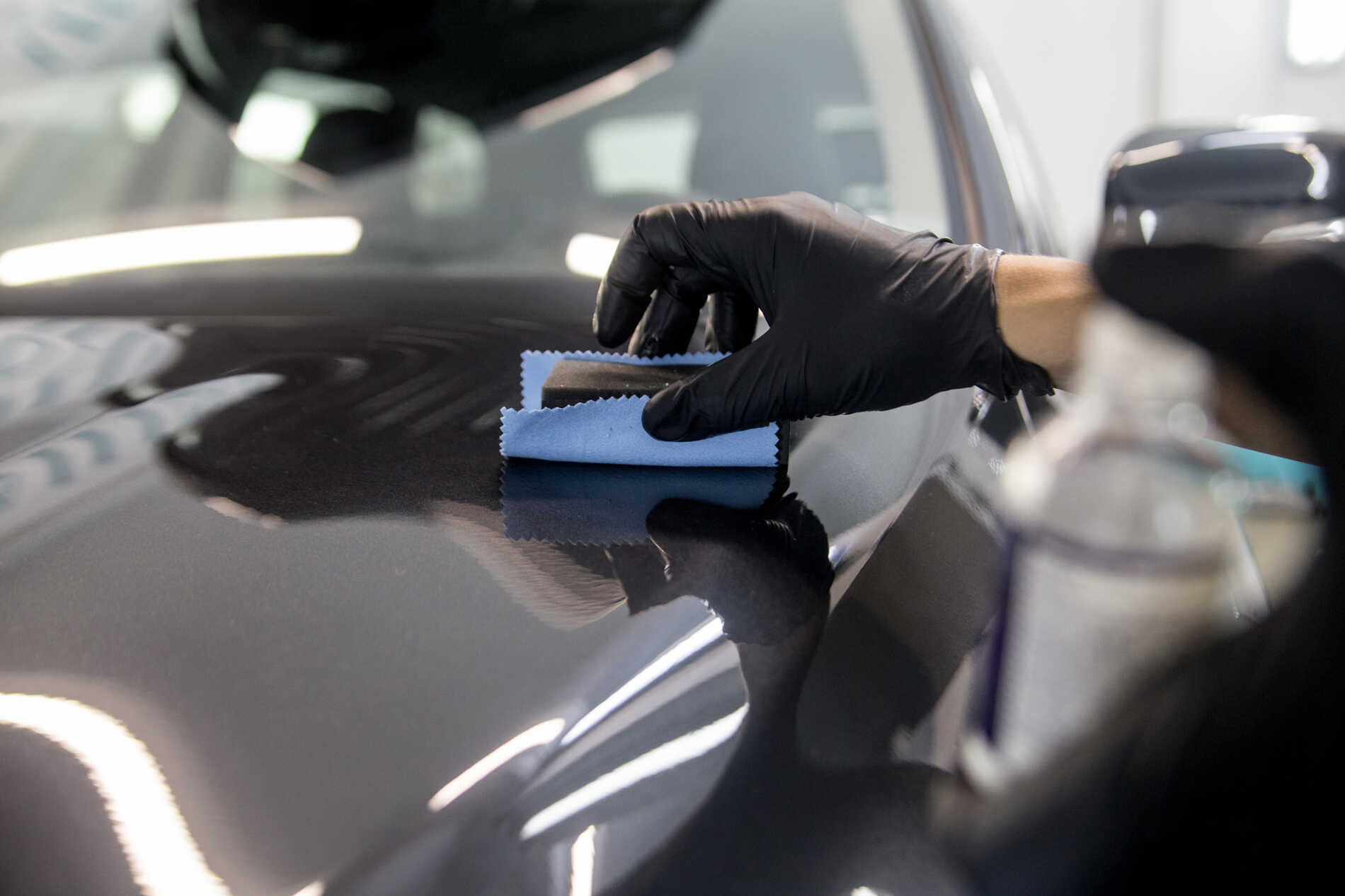 A person wearing black gloves is polishing the hood of a car.