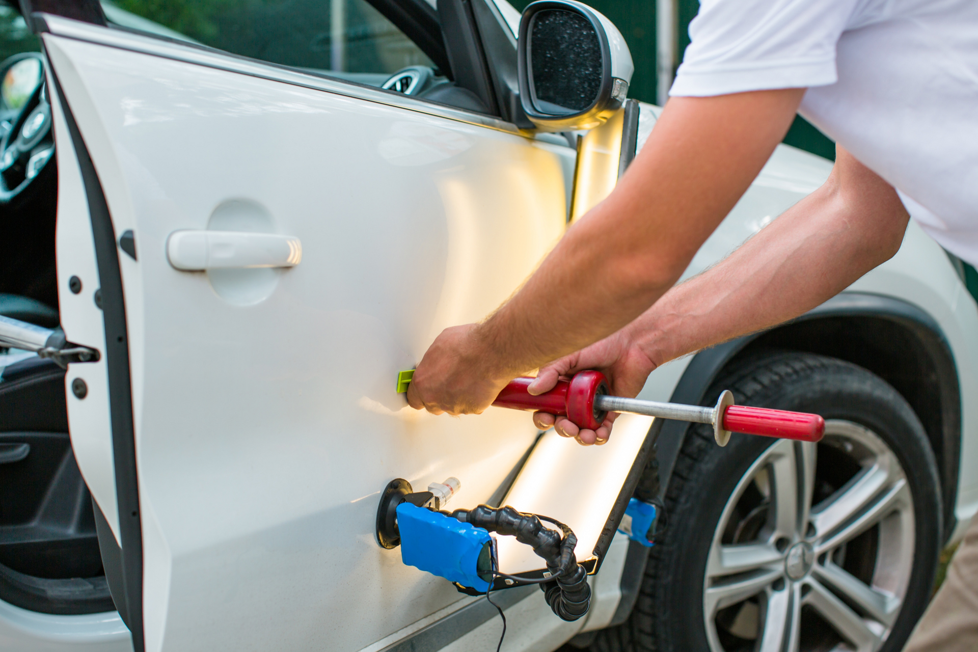 A man is working on a white car with a hammer.