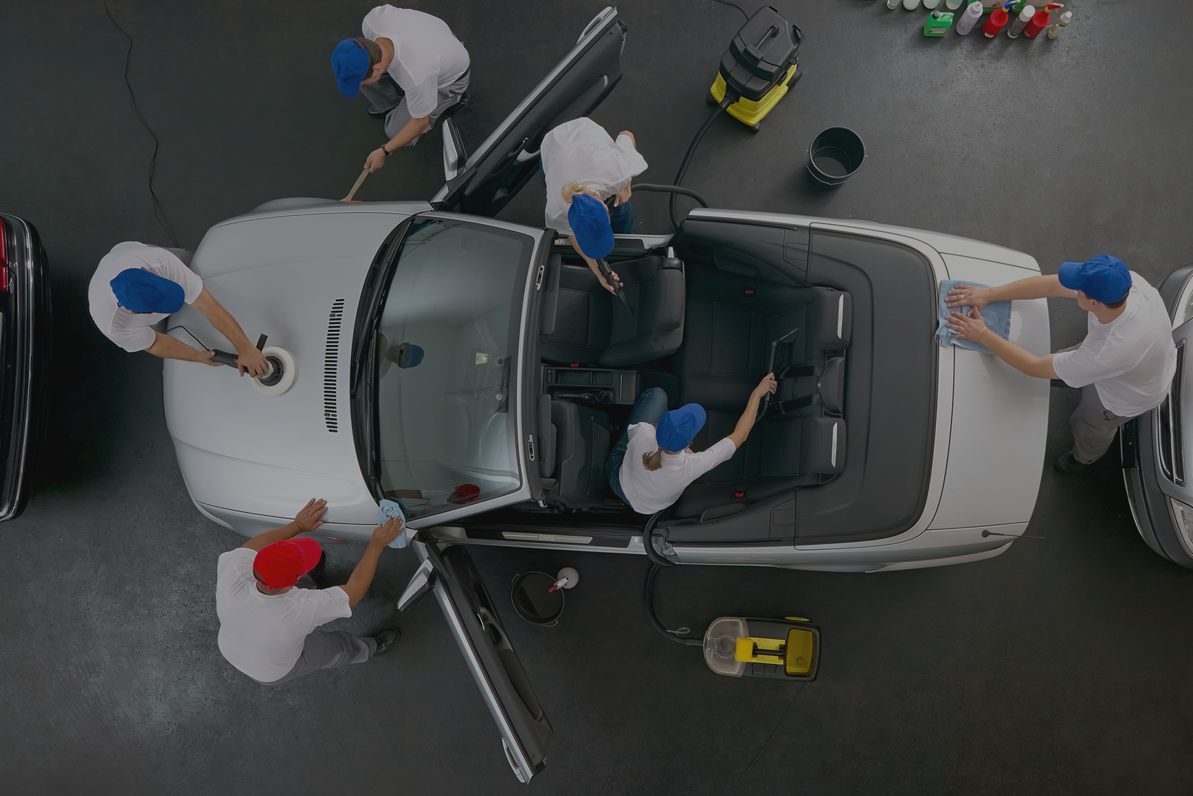 A group of men are cleaning a white car in a garage.