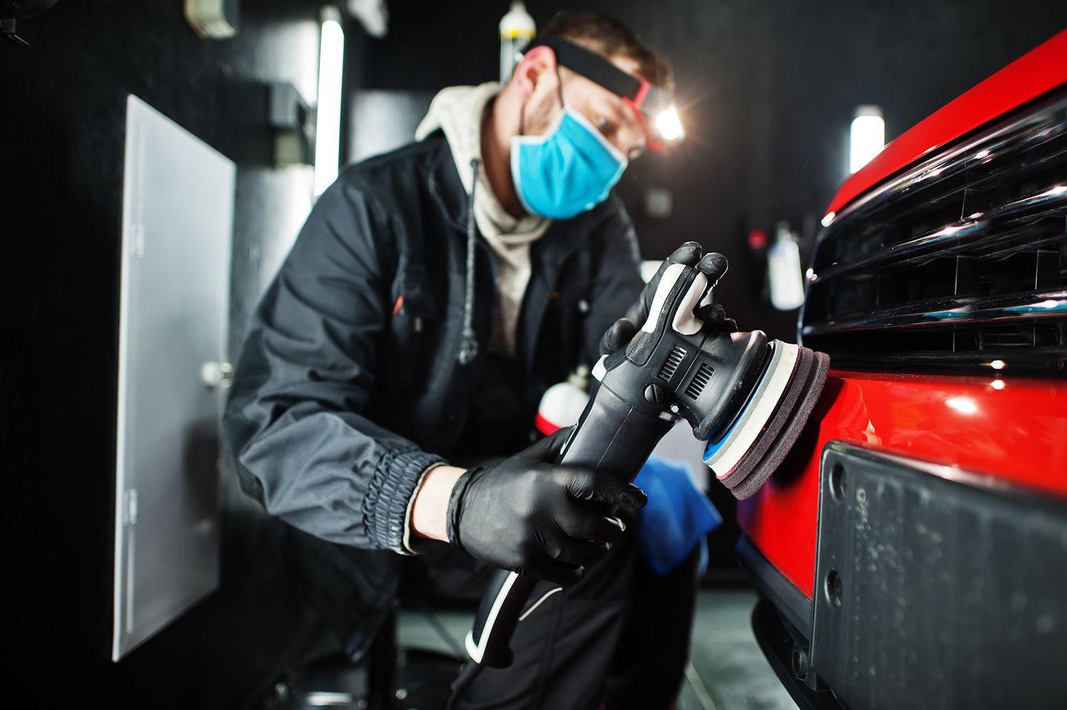 A man wearing a mask is polishing a red car.