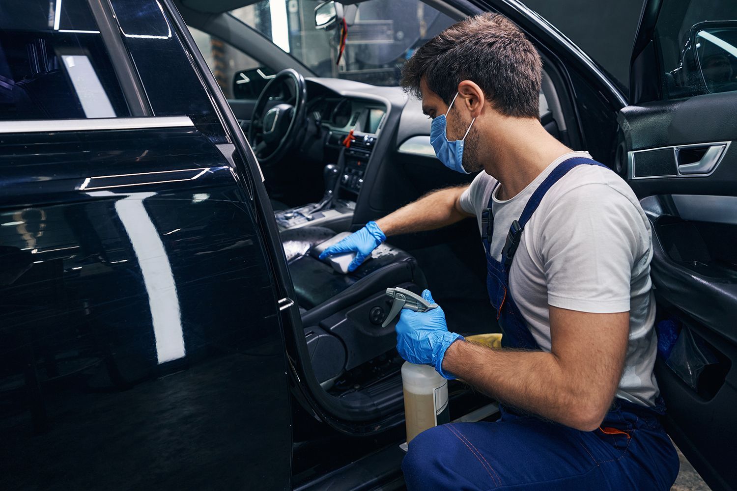 A man wearing a mask and gloves is cleaning the interior of a car.