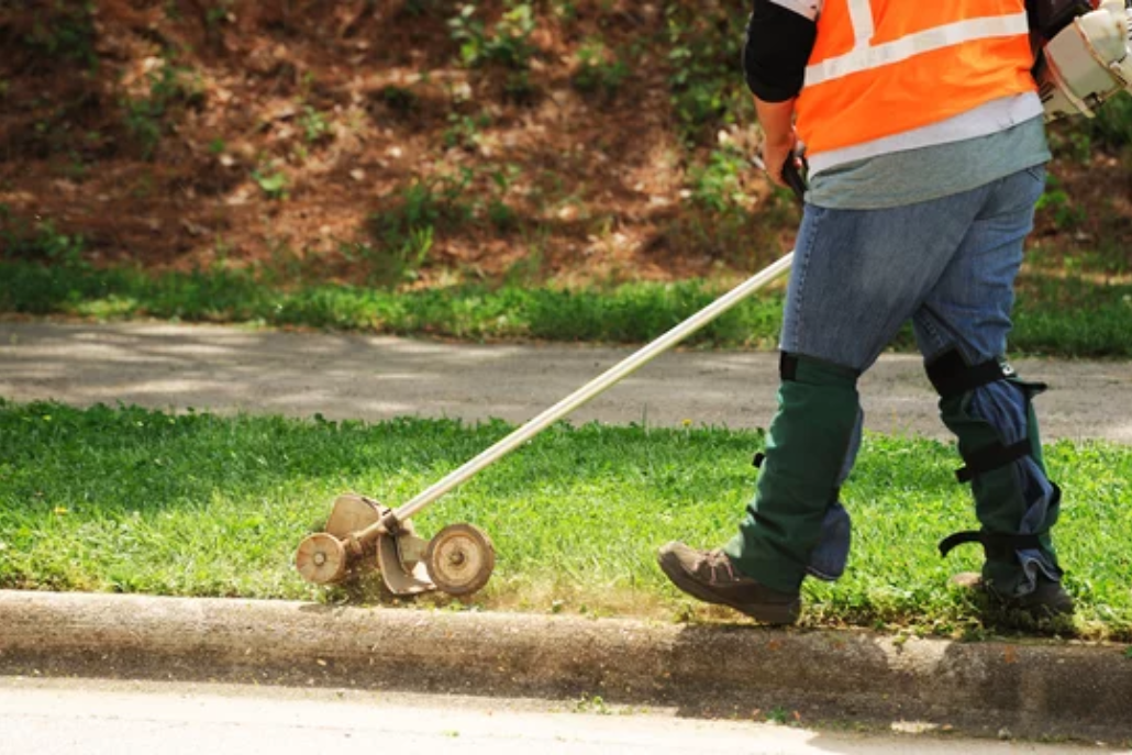 Person using a lawn edger to trim and define the edges of a lush green lawn.