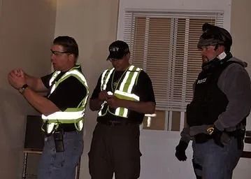 Three men wearing reflective vests are standing in a room.