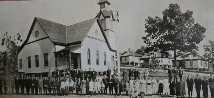 A black and white photo of a church with a large crowd gathered in front of it.