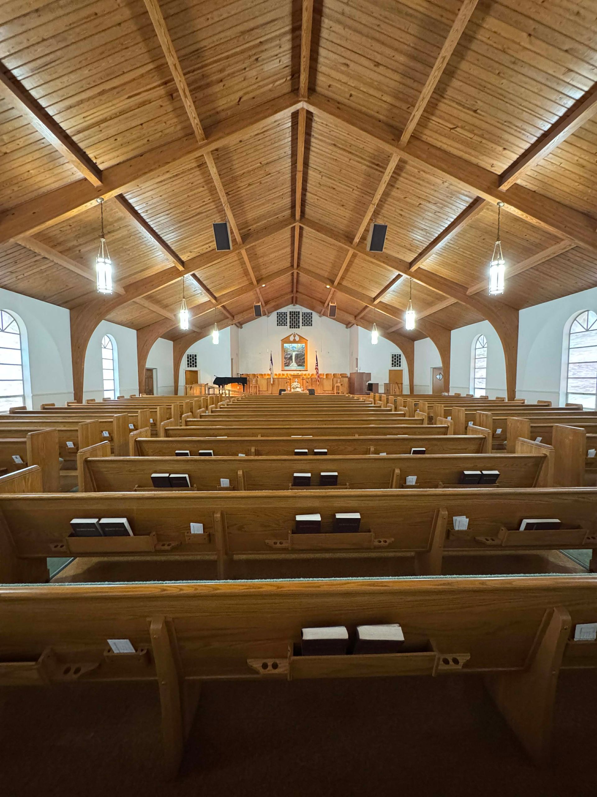 Interior of a church with rows of wooden pews leading to a raised altar under a wooden ceiling.