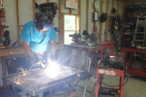 A man is welding a piece of metal in a garage.