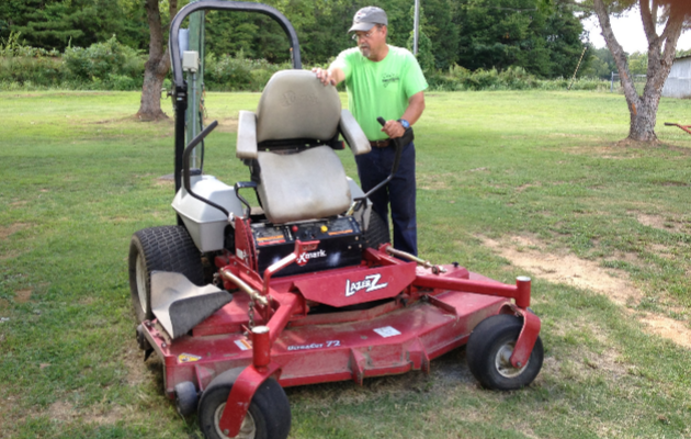 A man in a green shirt is standing next to a red lawn mower.