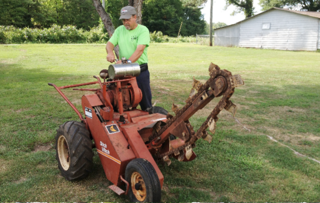 A man in a green shirt is driving a machine in a grassy field.
