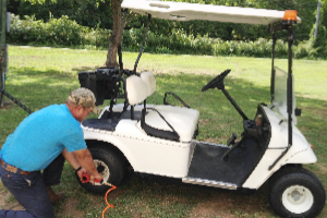 A man is kneeling down next to a white golf cart.