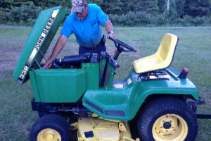 A man is working on a John Deere lawn mower.