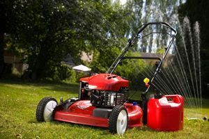 A red lawn mower is sitting on top of a lush green lawn next to a red gas can.