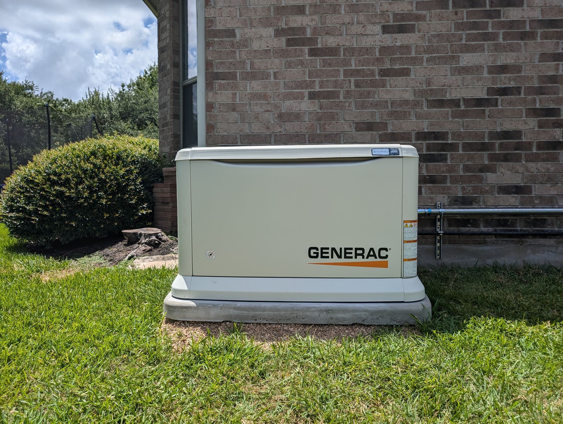 A generator is sitting in the grass next to a brick building.