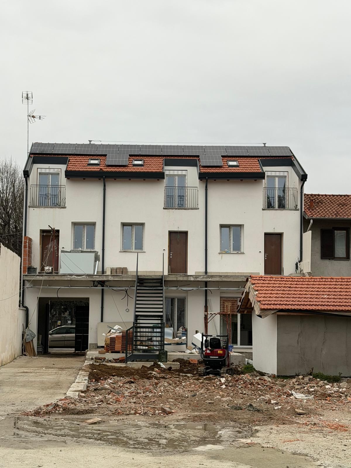 Edificio bianco a tre piani con tegole rosse sul tetto e un cortile sterrato antistante.