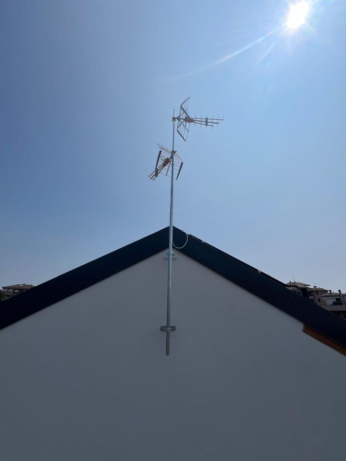 La cima di un edificio bianco con un'antenna sul tetto si staglia contro un cielo azzurro brillante e il sole.