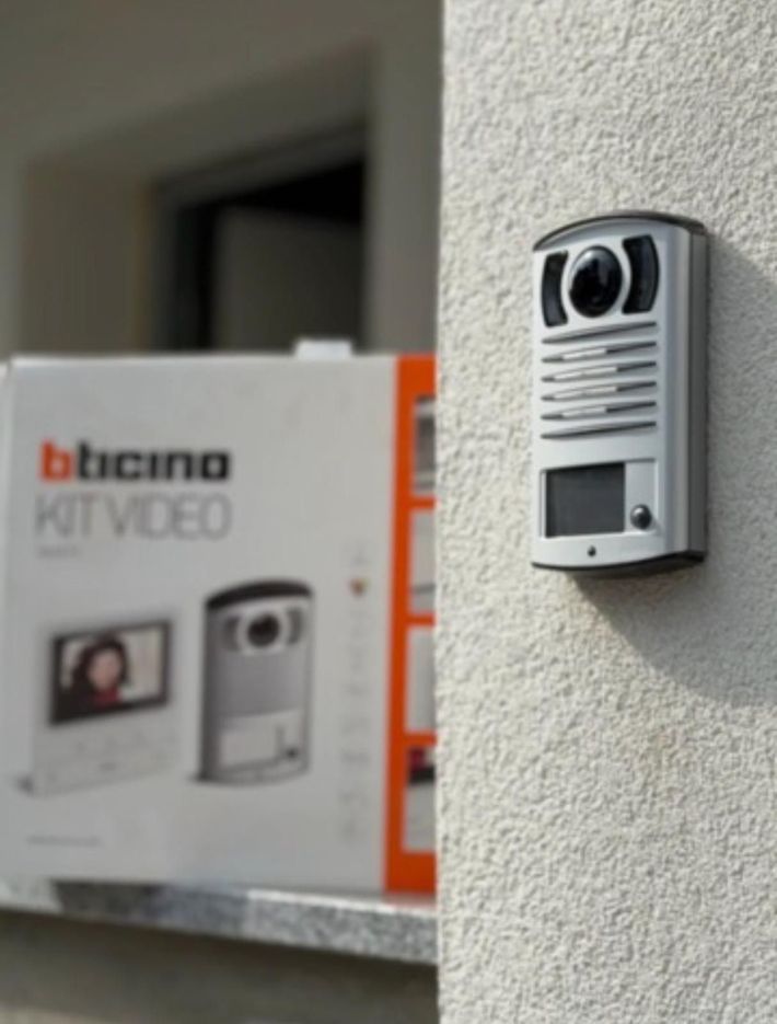 Videocitofono bianco a parete accanto a una scatola con l'etichetta 