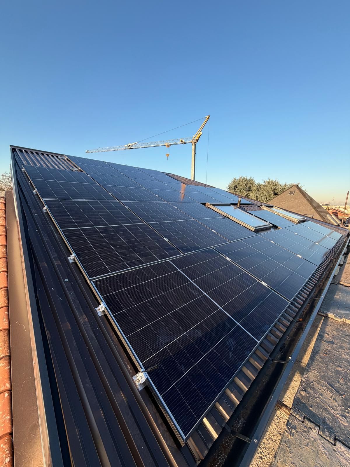 Pannelli solari installati su un tetto inclinato sotto un cielo azzurro e limpido, con una gru edile sullo sfondo.
