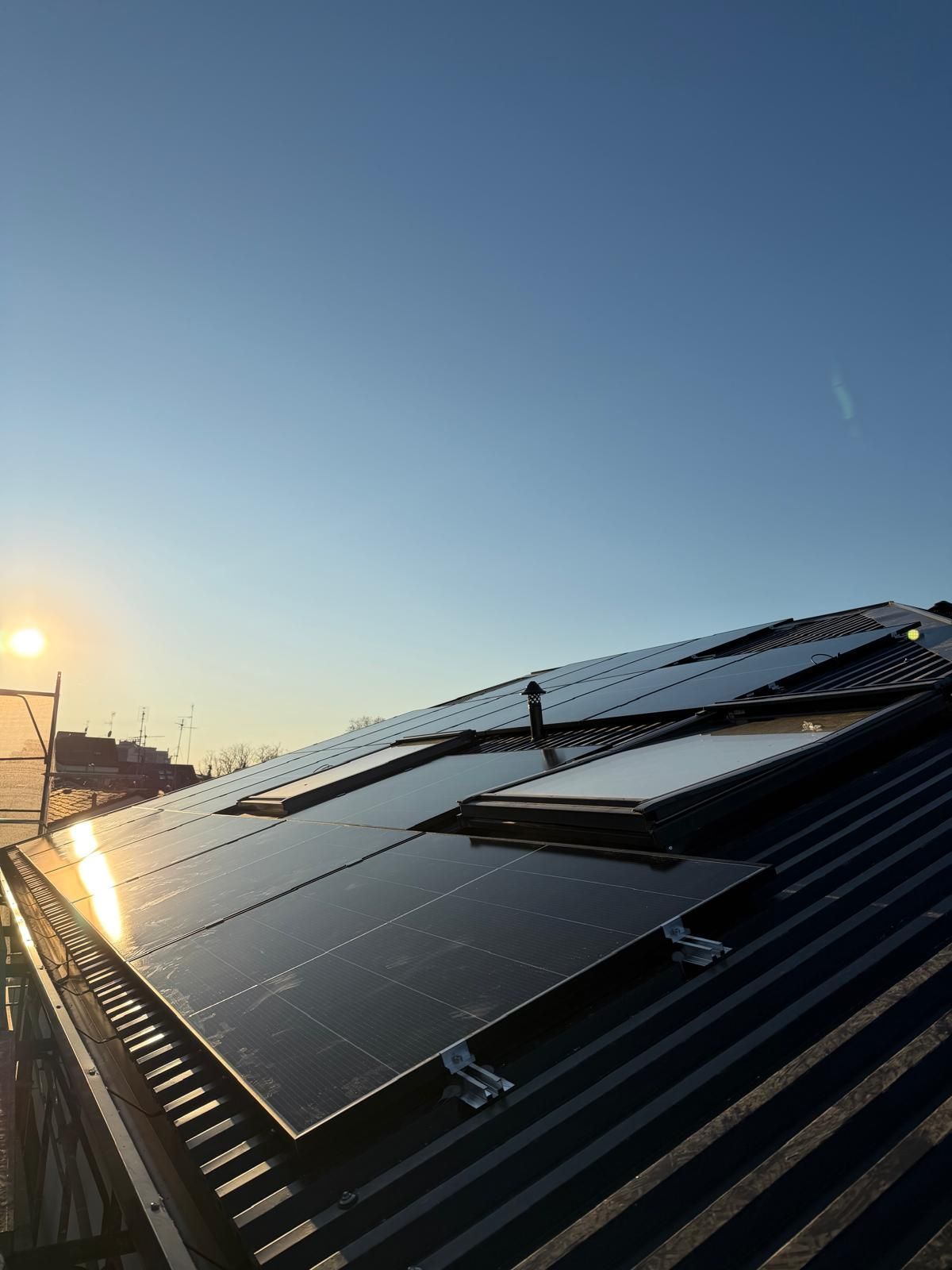 Pannelli solari su un tetto al tramonto, sotto un cielo azzurro e limpido.