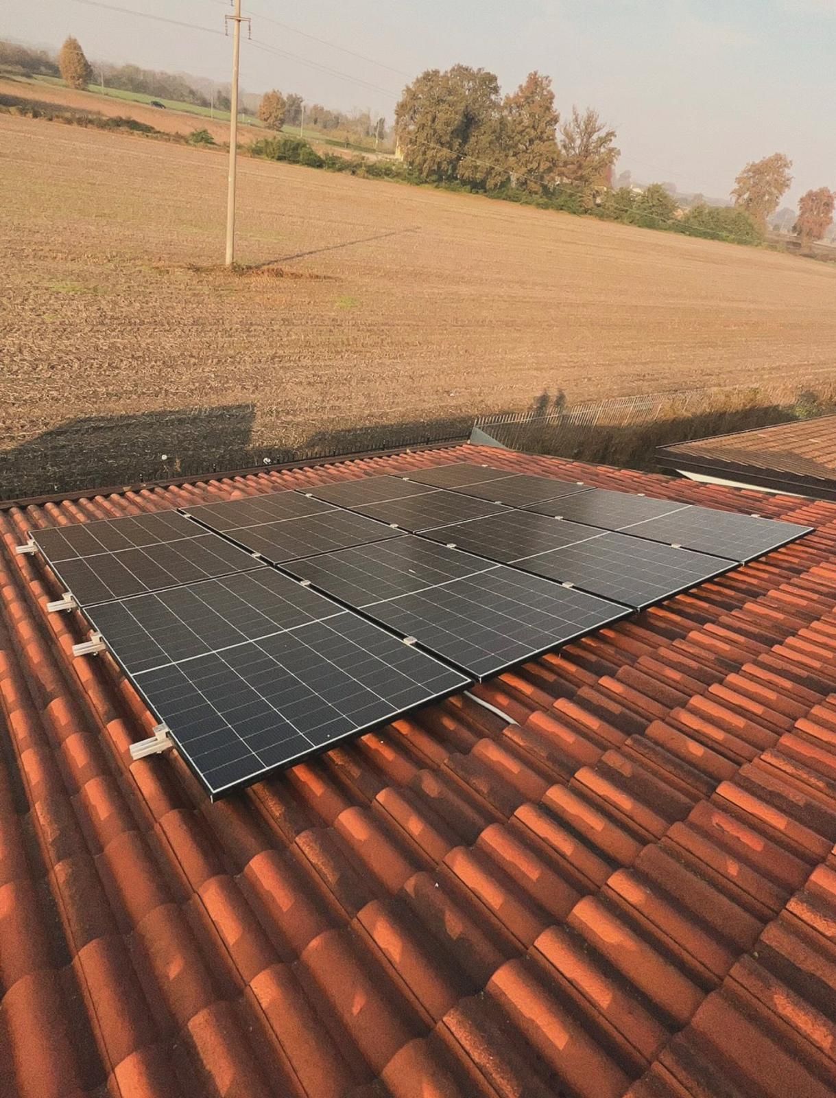 Pannelli solari installati su un tetto di tegole rosse, con un campo rurale sullo sfondo.