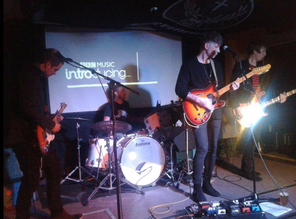 A group of men are playing guitars on a stage in front of a screen that says introducing