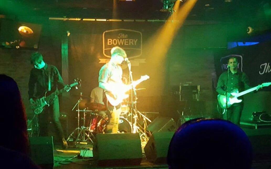 A group of people are playing instruments on a stage in front of a sign that says bowery.