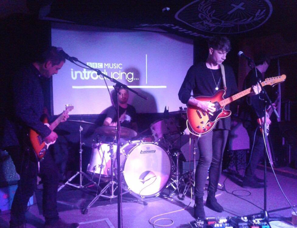 A man playing a guitar in front of a screen that says introducing