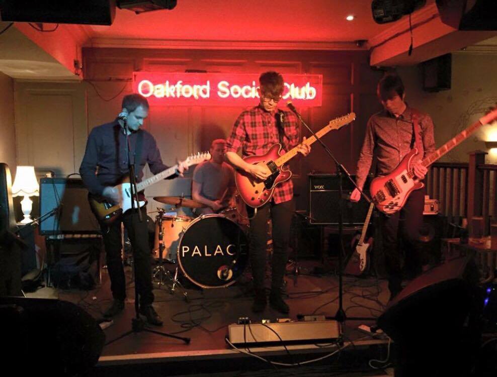 A group of men are playing guitars on a stage in front of a sign that says oakford sock club