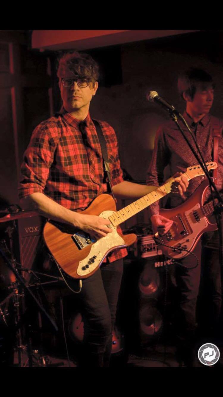 A man in a plaid shirt is playing a guitar on stage.