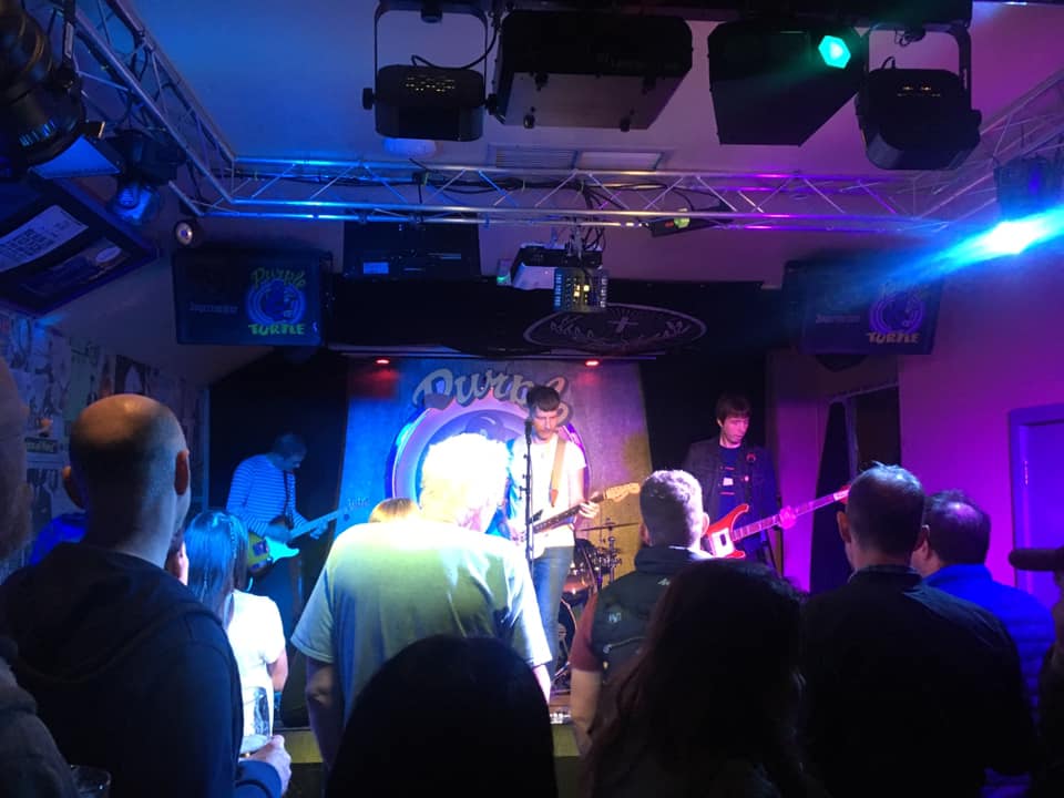 A group of people are standing in front of a stage watching a band perform.