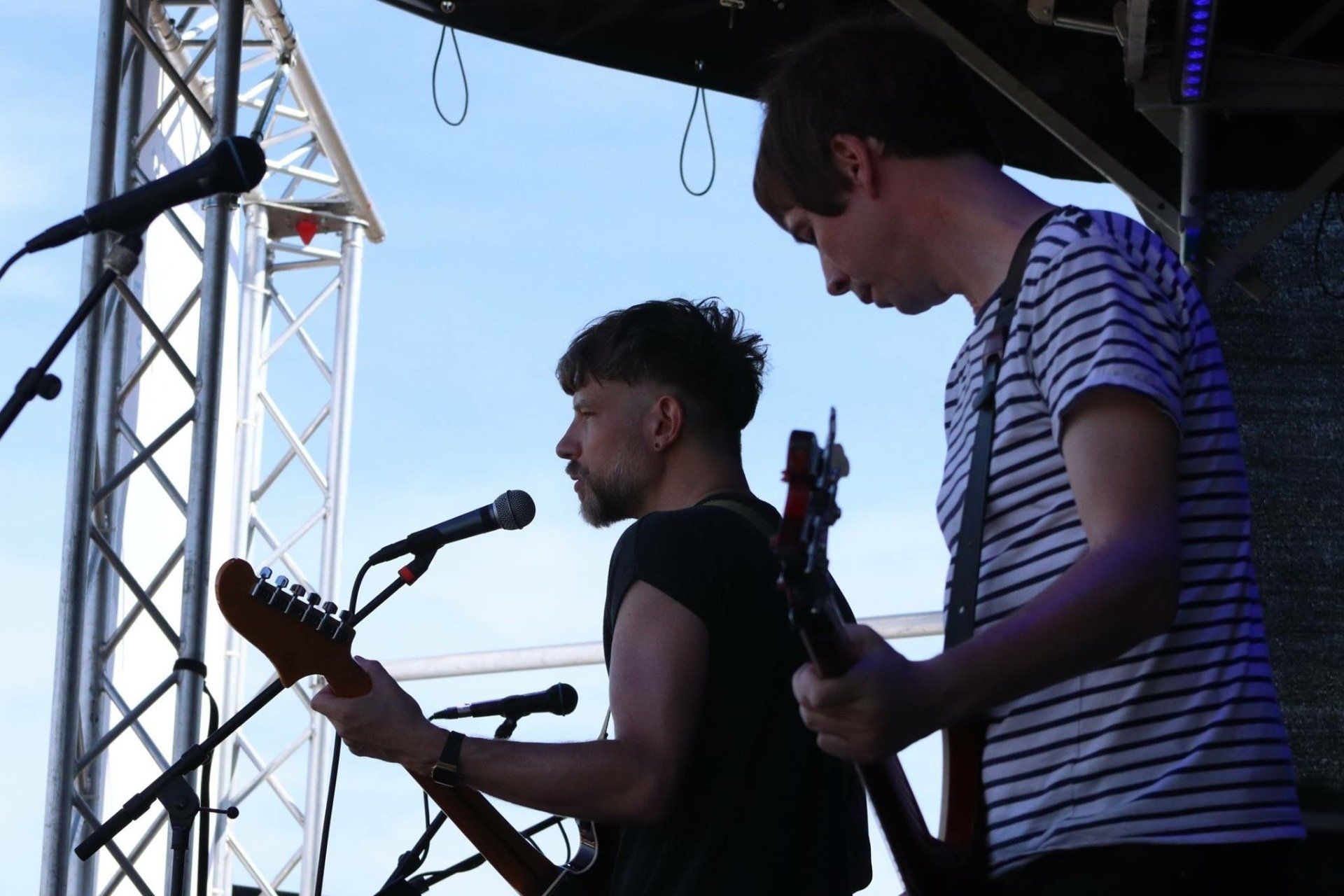 Two men are playing guitars and singing into microphones on a stage