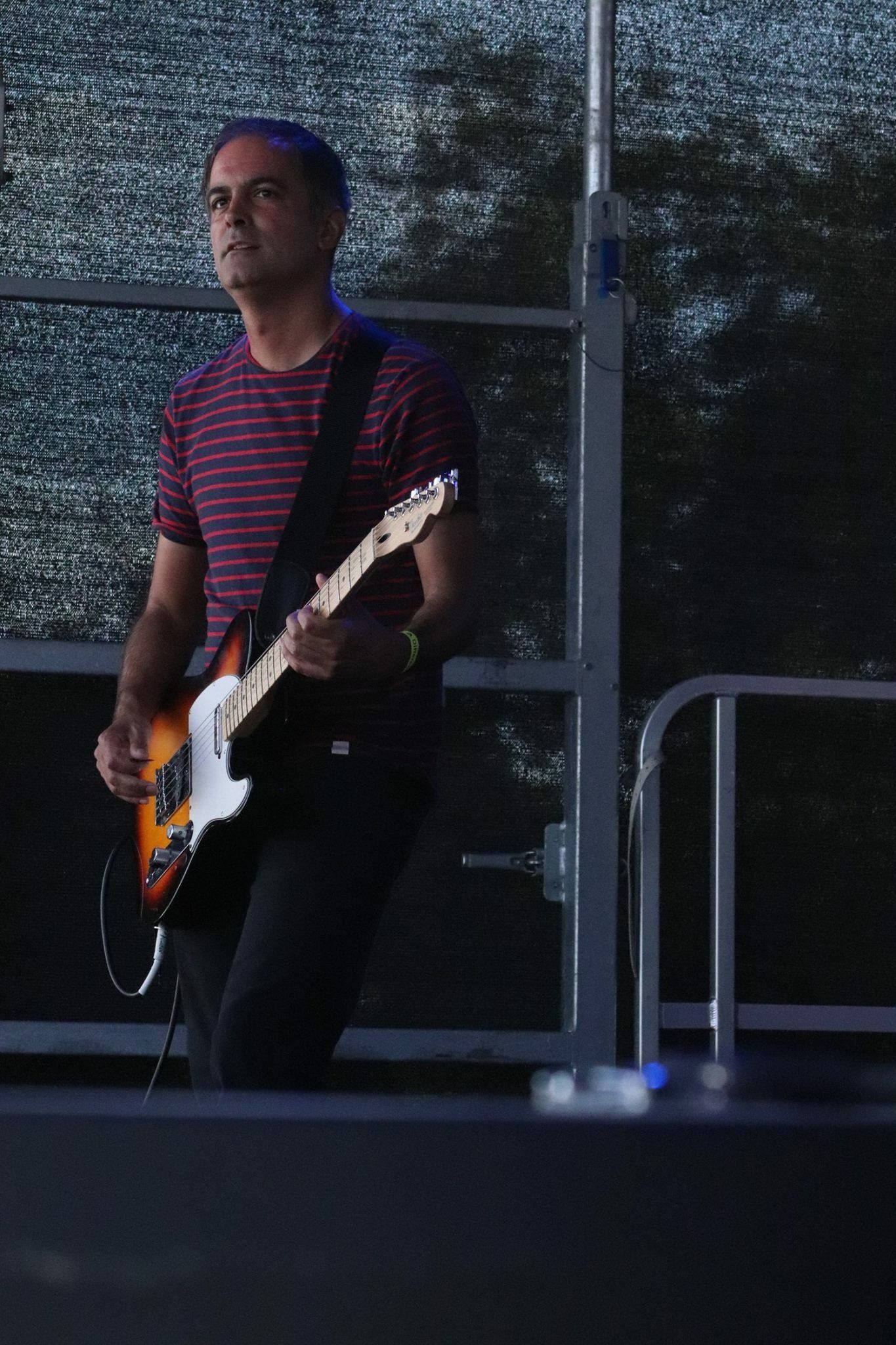 A man in a striped shirt is playing a guitar on a stage
