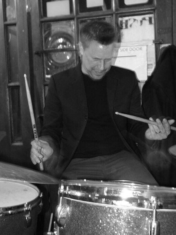 A man in a suit is playing drums in a black and white photo